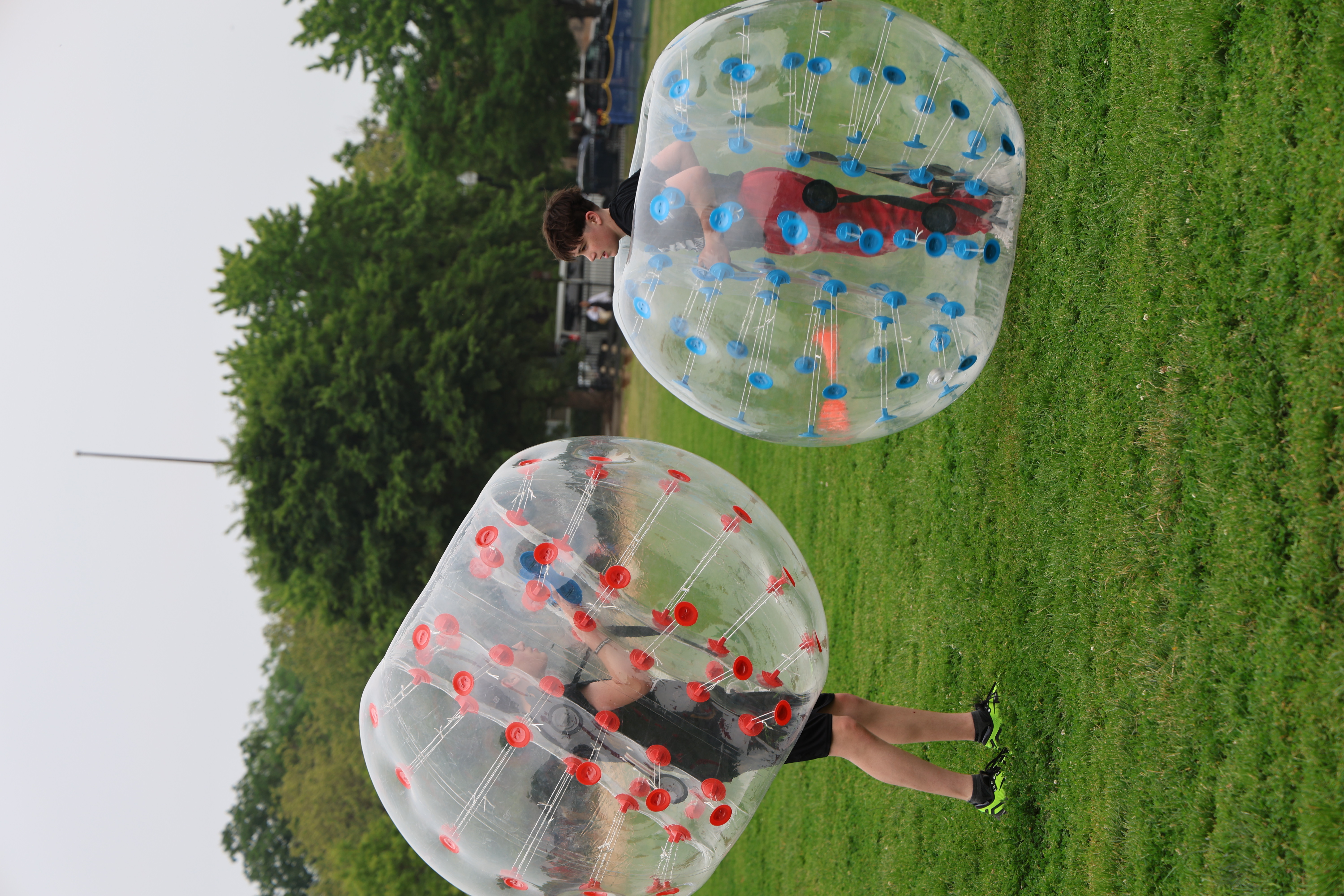 Two people in clear inflatable bumper balls on green grass.